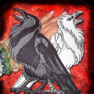 May include: Black and white embroidered raven and crow patch with a red glitter background. The patch features a black raven on the left and a white crow on the right, both with their beaks open and wings spread. The patch is available for purchase on the website SpiderStitches.com.