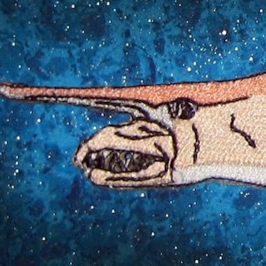 Peut inclure: Un requin brodé de couleur brun clair avec un long museau et plusieurs nageoires. Le requin nage sur un fond bleu avec des points blancs.