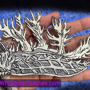 Può includere: Toppa ricamata bianca da stirare a forma di lumaca di mare con un design dettagliato di appendici ramificate. La toppa è su uno sfondo blu. WWW.SpiderStitches.com