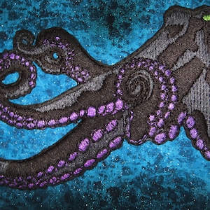 May include: Black embroidered octopus patch with purple accents on a blue background.