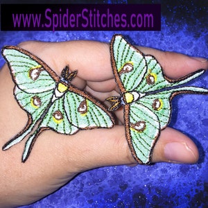 Pode incluir: Dois patches bordados de mariposa Luna, verde e marrom. As mariposas têm asas grandes e iridescentes com um padrão de olho amarelo e marrom.