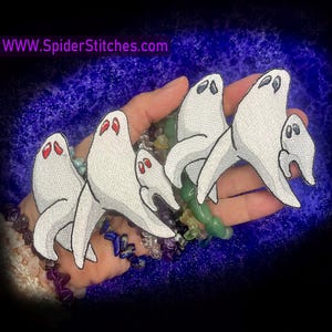 May include: Embroidered white ghost patches with red eyes and black outlines. The patches are in various sizes and shapes. The website address WWW.SpiderStitches.com is in the upper left corner. These patches are perfect for Halloween or spooky-themed crafts.