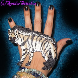 May include: A black and white striped embroidered patch of a hyena on a hand wearing a bracelet with colorful stones.