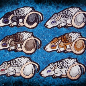May include: Six embroidered patches of sleeping winged rats in various colors, including gray, brown, and white. The patches are on a blue background with a glittery texture.