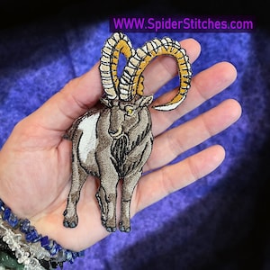 May include: Embroidered patch of a mountain goat, rendered in brown, white, and gold thread. The patch highlights the goat's curved horns and detailed features. The text "WWW.SpiderStitches.com" is displayed in the upper right corner of the patch.