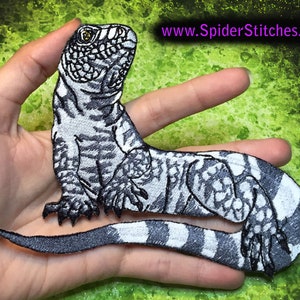 Peut inclure: Patch brodé noir et blanc d'un lézard avec une queue rayée. Le patch mesure environ 12,5 cm de long et est tenu dans une main.