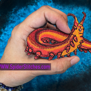 May include: An embroidered iron-on patch of a red and orange cartoon creature with a curled tail and multiple legs. The patch is on a blue background. WWW.SpiderStitches.com