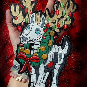 May include: A white skeleton reindeer wearing a green wreath with red and gold ornaments and a red bow. The reindeer has antlers with red and green lights.