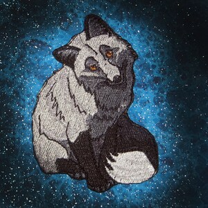 Puede incluir: Un zorro bordado en plata y negro sobre un fondo blanco. El zorro está sentado con la cola enroscada alrededor de su cuerpo.