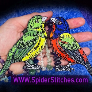 May include: Two embroidered bird patches. One is green and yellow, the other is blue, red, and green. The patches are held in a hand, with a beaded bracelet and the text "WWW.SpiderStitches.com" in the image.