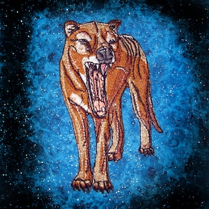Pode incluir: Uma imagem bordada de um tigre da Tasmânia rosnando, em tons de marrom e bege, sobre um fundo estrelado azul e preto.