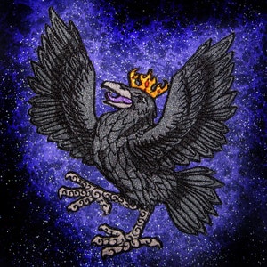 Pode incluir: Um corvo preto com uma coroa dourada, em pé sobre um fundo de galáxia azul e roxo.