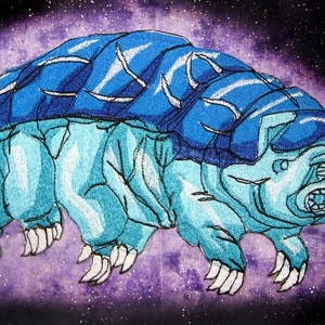 May include: Embroidered patch depicting a blue and light blue tardigrade, or water bear, set against a purple and gold speckled backdrop. The design showcases detailed stitching and a distinctive style.
