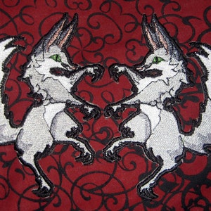 May include: Two embroidered gray foxes facing each other with their tails curled. The foxes are on a red background with black swirls.