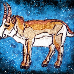 May include: Embroidered image of a brown and white antelope with long horns against a blue starry background.
