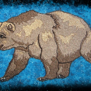 Può includere: Orso marrone ricamato che cammina su uno sfondo blu con glitter bianco.