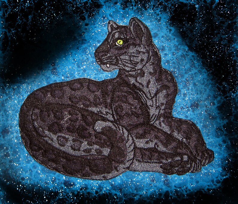 May include: A black panther with a spotted pattern is lying down on a blue background with white speckles. The panther has a yellow eye.