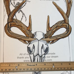 May include: Iron-on patch of a white deer skull with brown antlers. The patch is approximately 4 inches tall. The text "Iron on Patch" and "www.spiderstitches.com" is printed on the white background.