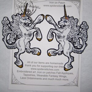 May include: Two white iron-on patches of a unicorn with gold horns and hooves. The unicorns are facing opposite directions and have a swirling cloud-like design. The text "Iron on Patch" and "www.spiderstitches.com" is at the top of the image. The text "All of our items are homemade thank you for supporting our dream www.spiderstitches.com Embroidered art, Iron on patches Felt Appliques, Tapestries, Wearable Fantasy Wings, Lace Ordainments and much much more." is at the bottom of the image.