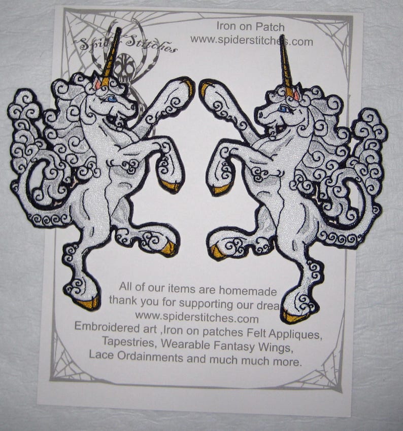 May include: Two white iron-on patches of a unicorn with gold horns and hooves. The unicorns are facing opposite directions and have a swirling cloud-like design. The text "Iron on Patch" and "www.spiderstitches.com" is at the top of the image. The text "All of our items are homemade thank you for supporting our dream www.spiderstitches.com Embroidered art, Iron on patches Felt Appliques, Tapestries, Wearable Fantasy Wings, Lace Ordainments and much much more." is at the bottom of the image.