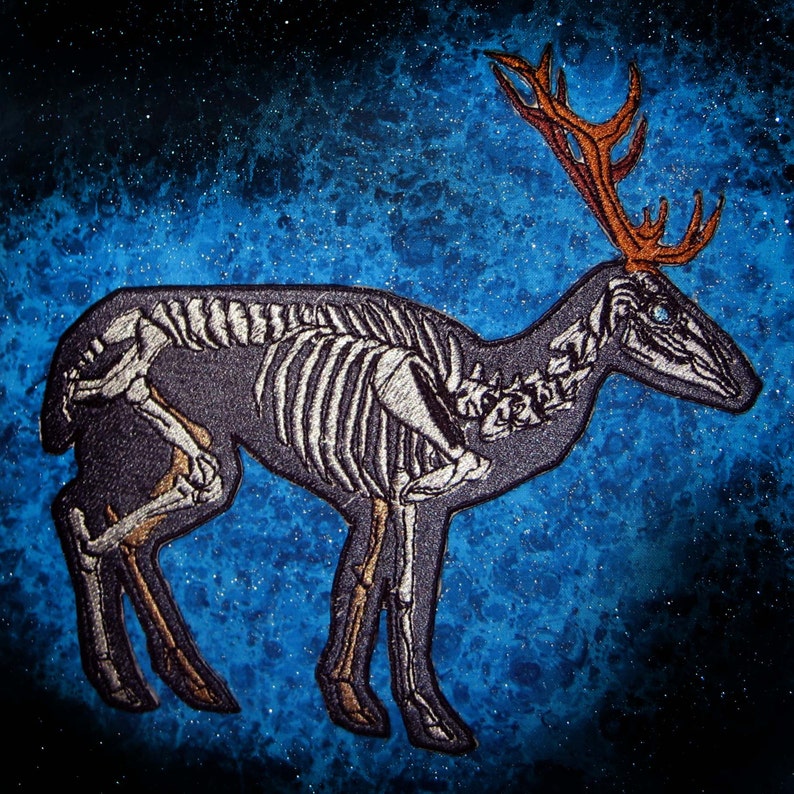 May include: A black and white embroidered patch of a deer skeleton with antlers against a blue starry background.