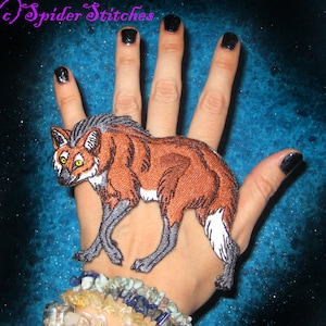 Könnte beinhalten: Ein gestickter Aufnäher eines Mähnenwolfes, einer Art Wildhund, auf einer Hand. Der Aufnäher ist etwa 10 cm lang und 7,5 cm breit.