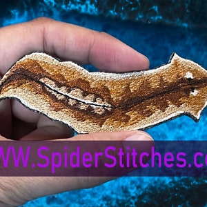 以下が含まれることがあります： 手前の「WWW.SpiderStitches.com」というテキストが入った、茶色と白の刺繍パッチで葉っぱが描かれている