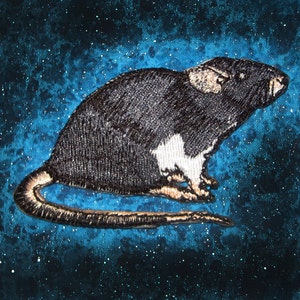 以下が含まれることがあります： 青と黒の斑点のある背景に、黒と白の刺繍されたネズミがいます