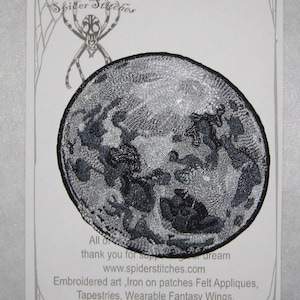 May include: A black and white embroidered iron-on patch depicting a stylised image of the Earth. The patch is surrounded by a spider web design and the text "Iron on Patch" and "www.spiderstitches.com".