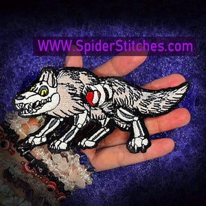 May include: Embroidered patch featuring a skeletal wolf design with a red heart. The patch has a black border and is set against a dark background. The website address "WWW.SpiderStitches.com" is displayed in a purple rectangle.