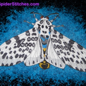May include: A detailed illustration of a moth with white wings speckled with black spots. The moth has a yellow and black body, and the background is a textured blue and black. The website address "www.SpiderStitches.com" is visible at the top.