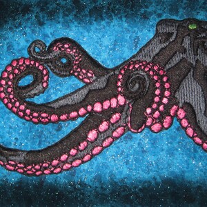 May include: Embroidered patch of a black octopus with pink tentacles on a blue background.