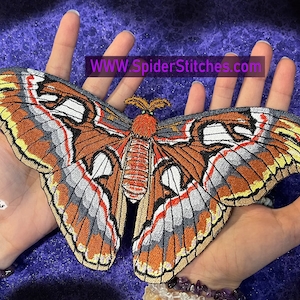 May include: A large, embroidered butterfly patch with intricate details in shades of brown, orange, yellow, gray, and white. The patch has a detailed design and the text "WWW.SpiderStitches.com".