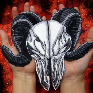 May include: An embroidered ram skull with black horns. The skull is detailed with intricate stitching and the horns are curled.