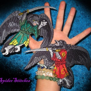 May include: Two embroidered iron-on patches depicting black crows wielding swords. The crow on the left is adorned in a green and yellow outfit, while the crow on the right is dressed in a red and yellow ensemble. Both crows have an aggressive expression.