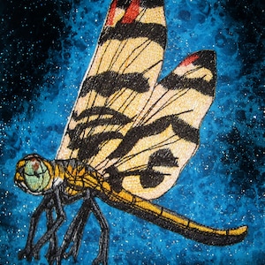 May include: A yellow and black dragonfly with red accents is embroidered on a blue background with white speckles. The dragonfly's wings are spread out and its body is facing to the left.