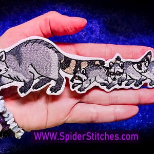 Könnte beinhalten: Ein Set mit fünf gestickten Waschbär-Aufnähern. Die Aufnäher sind grau und schwarz mit weißen Akzenten. Der größte Aufnäher zeigt einen Waschbären beim Gehen, die anderen vier Aufnäher zeigen Waschbären in verschiedenen Posen. Die Aufnäher sind auf weißem Hintergrund.