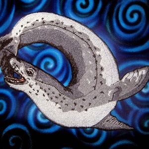 Op de afbeelding: Gestikte patch van twee grijze zeehonden, een bijt in de staart van de ander, op een blauwe achtergrond met draaiende patronen.