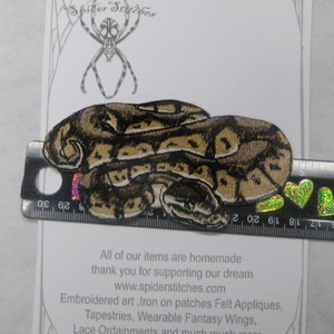 May include: Iron-on patch depicting a coiled brown and green snake with a textured surface. The patch measures approximately 7.5 cm in length. The text "Iron on Patch" and "www.spiderstitches.com" is printed on the white background.