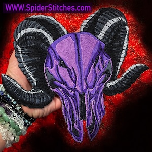 May include: Purple embroidered ram skull patch with black horns.  The patch is held in a hand with bracelets.  www.SpiderStitches.com