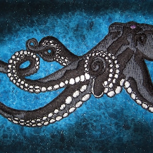 May include: A black octopus with white spots embroidered on a blue sparkly background.