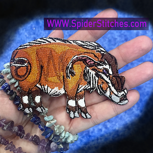 May include: Embroidered patch of a brown and white boar with a large tusk and a purple eye. The patch is on a hand with a blue background. The text "WWW.SpiderStitches.com" is visible at the top of the image.