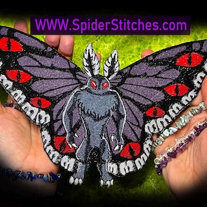 Puede incluir: Un parche bordado grande con un diseño de Mothman con alas moradas y negras, ojos rojos y un cuerpo gris. El parche se sostiene en las manos, con la dirección del sitio web "WWW.SpiderStitches.com" visible en la parte superior.