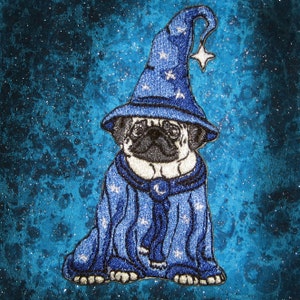 Puede incluir: Un pug blanco con un sombrero de mago azul y una túnica con estrellas. El fondo es una tela azul brillante.