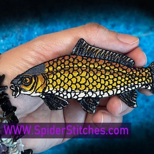 Puede incluir: Un parche de hierro bordado de un pez carpa dorado y negro. El pez tiene la barriga blanca y las aletas negras. El parche mide aproximadamente 10 cm de largo.