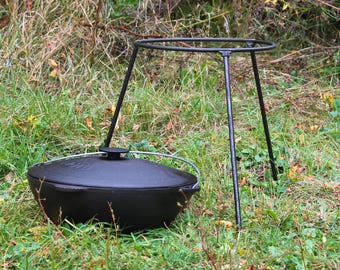 Peut inclure: Une marmite en fonte noire avec un couvercle est posée sur un trépied en métal noir. La marmite et le trépied sont sur un lit d'herbe verte.