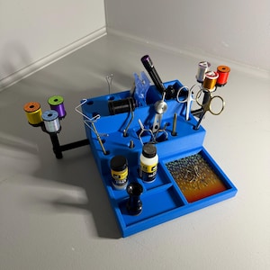 May include: Blue fly tying station with various tools and materials, including spools of thread, scissors, bobbins, and bottles of fly tying wax.