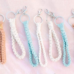 May include: Six colourful crocheted keychains with silver key rings. The keychains are made with a variety of colours, including beige, white, and light blue.