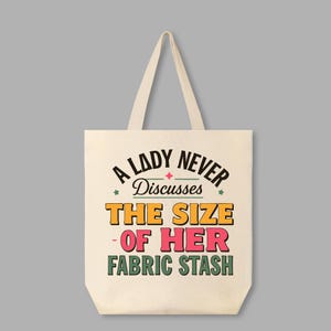 May include: A white canvas tote bag with a retro-style design that says "A Lady Never Discusses The Size Of Her Fabric Stash".