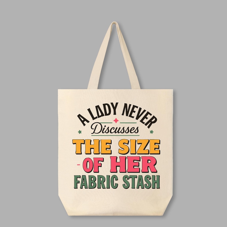 May include: A white canvas tote bag with a retro-style design that says "A Lady Never Discusses The Size Of Her Fabric Stash".